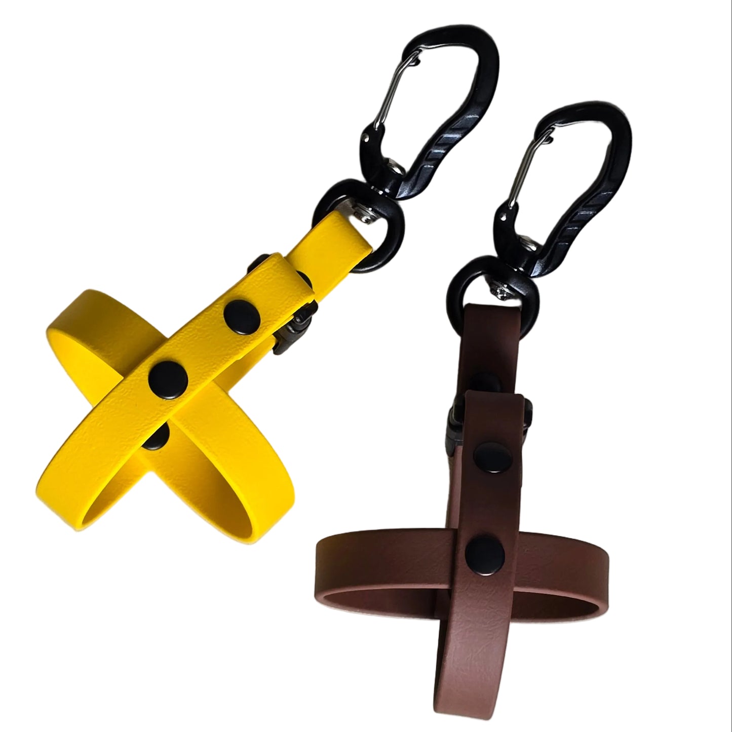A clean studio photograph on a white background showing two handcrafted BioThane dog ball holders. On the left is a vibrant yellow BioThane holder with black hardware and rivets, and on the right is a deep brown BioThane holder with matching black hardware and rivets. Both are equipped with high-strength black aluminum carabiners for easy attachment to gear, demonstrating a durable and hygienic way to carry fetch balls hands-free. No balls are included with these specific holders.